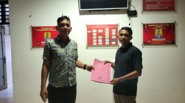 Seorang pria sedang berdiri di depan kantor polisi sambil menunjukkan berkas laporan, melaporkan dugaan pemerasan oleh debt collector. (Foto: Istimewa)