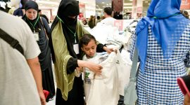 Seorang anak yatim dengan penuh semangat memilih pakaian baru didampingi oleh panitia dalam program 