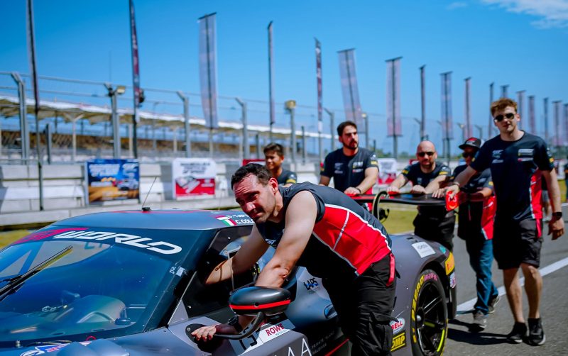 Sejumlah kru teknis dari tim balap mendorong mobil sport menuju area lintasan balap. Dengan ekspresi serius dan penuh fokus, mereka bekerja sama memastikan kendaraan dalam kondisi siap tempur, mencerminkan kerja tim dan semangat kompetisi yang tinggi di ajang balap internasional. (Foto: Dok. PLN)