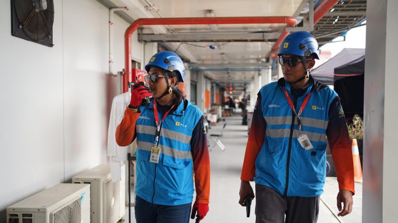 Dua petugas PLN mengenakan alat pelindung diri lengkap saat menjalankan tugas pengawasan sistem kelistrikan di lapangan. Komunikasi aktif melalui radio menjadi bagian penting dalam memastikan operasional berjalan aman dan lancar. (Foto: Dok. PLN)