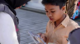 Seorang anak antusias membaca buku yang dibagikan relawan Program Desa Berdaya PLN NTB dalam kampanye literasi di Desa Medana. (Dok. PLN)