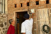 Caption: Petugas PLN memastikan sambungan listrik di rumah warga telah terpasang sebagai bagian dari program kepedulian YBM PLN.(Foto: Istimewa 